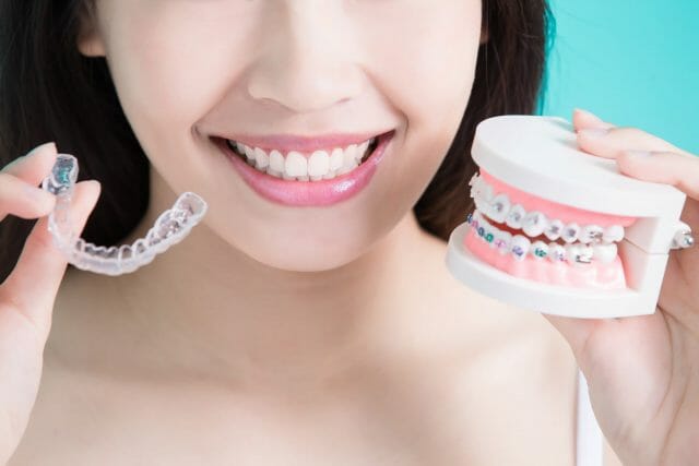 Woman holding up invisible aligners and model of braces 